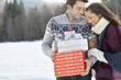 Smiling couple hugging and holding Christmas gifts in snow