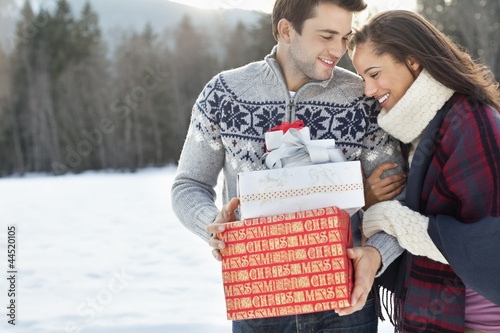 Photo: Smiling couple hugging and holding Christmas gifts in snow Smiling couple hugging and holding Christmas gifts in snow