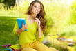 Young beautiful woman lays on green field and reads book.