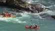 Yellow canoe paddling in the sea through a gap in some rocks.
