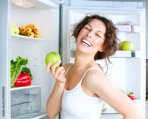 Photo: Beautiful Young Woman near the Refrigerator with fresh apple Beautiful Young Woman near the Refrigerator with fresh apple