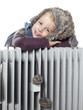 Foto: Cute girl with pelt cap leans over a radiator to keep warm Cute girl with pelt cap leans over a radiator to keep warm