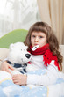 Little sick girl with thermometer embraces toy bear in bed