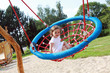 Mädchen sitzt in einer Nestschaukel auf einem Spielplatz