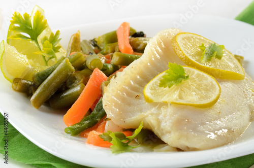 Photo: Tilapia fish baked with herbs and lime served on white plate wit Tilapia fish baked with herbs and lime served on white plate wit