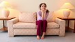 Woman sits on sofa with head on her hand