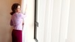 Young woman draws curtains and opens window