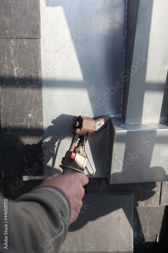Photo: Manual worker using tool to melt lead around window Manual worker using tool to melt lead around window