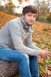 Outdoors portrait of happy young man sitting in autumn park