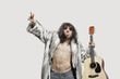 Foto: Young man in fur coat holding guitar while gesturing over gray background Young man in fur coat holding guitar while gesturing over gray background