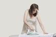 Young woman ironing shirt against gray background