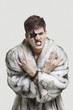 Photo: Portrait of frustrated young man in fur coat clenching teeth and making rebellious gesture against gray background Portrait of frustrated young man in fur coat clenching teeth and making rebellious gesture against gray background