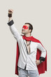 Young man in superhero costume with hand raised against gray background