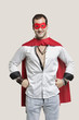 Photo: Portrait of young man in superhero costume with hands on hip standing against gray background Portrait of young man in superhero costume with hands on hip standing against gray background