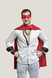 Photo: Portrait of young man in superhero costume with hands on hip standing against gray background Portrait of young man in superhero costume with hands on hip standing against gray background