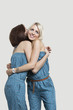 Photo: Two young female friends in matching jump suits hugging each other over gray background Two young female friends in matching jump suits hugging each other over gray background