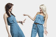 Photo: Two surprised women wearing similar jump suits looking at each other over gray background Two surprised women wearing similar jump suits looking at each other over gray background
