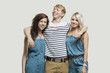 Photo: Portrait of two young women in similar jumpsuits standing with happy male friend over gray background Portrait of two young women in similar jumpsuits standing with happy male friend over gray background