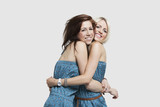 Photo: Two young women in matching jump suits embracing each other over gray background Two young women in matching jump suits embracing each other over gray background