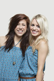 Photo: Portrait of two young women in similar jump suits smiling over gray background Portrait of two young women in similar jump suits smiling over gray background