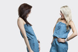 Photo: Two shocked women wearing matching jump suits looking at each other over gray background Two shocked women wearing matching jump suits looking at each other over gray background