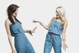 Photo: Two surprised women wearing similar jump suits looking at each other over gray background Two surprised women wearing similar jump suits looking at each other over gray background