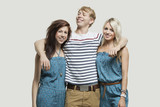 Photo: Portrait of two young women in similar jumpsuits standing with happy male friend over gray background Portrait of two young women in similar jumpsuits standing with happy male friend over gray background