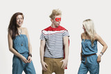 Photo: Young man in superhero costume standing with happy female friends in matching jump suits against gray background Young man in superhero costume standing with happy female friends in matching jump suits against gray background