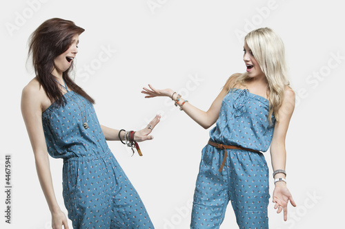 Photo: Two surprised women wearing similar jump suits looking at each other over gray background Two surprised women wearing similar jump suits looking at each other over gray background
