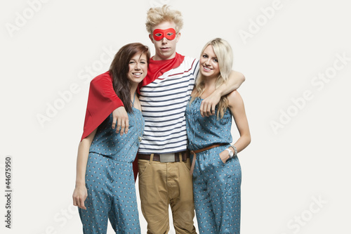 Photo: Portrait of young man in superhero costume and women wearing jumpsuits standing together against gray background Portrait of young man in superhero costume and women wearing jumpsuits standing together against gray background