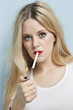 Photo : Portrait of young blond woman igniting cigarette against light blue background Portrait of young blond woman igniting cigarette against light blue background