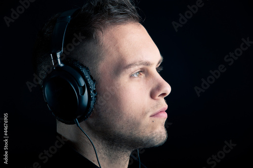Photo: Close up profile of man with ear-phones on black background. Close up profile of man with ear-phones on black background.