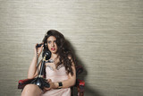 Photo: Attractive young woman using nostalgic telephone while sitting on chair against textured background Attractive young woman using nostalgic telephone while sitting on chair against textured background