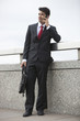 Photo: Young Indian businessman using cell phone with laptop bag by parapet Young Indian businessman using cell phone with laptop bag by parapet