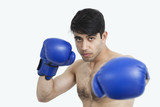 Photo: Portrait of an Indian shirtless man wearing blue boxing gloves against gray background Portrait of an Indian shirtless man wearing blue boxing gloves against gray background