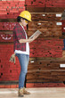 Photo: Side view of an Asian female industrial worker using tablet PC with stacked wooden planks in background Side view of an Asian female industrial worker using tablet PC with stacked wooden planks in background