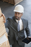 Photo: High angle view of African American male contractor inspecting wooden planks while holding tablet PC High angle view of African American male contractor inspecting wooden planks while holding tablet PC
