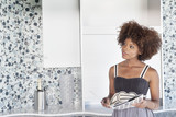 Photo: Young African American woman looking at designed wall as she holds design swatches Young African American woman looking at designed wall as she holds design swatches