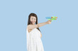 Photo: Happy young woman aiming with a toy gun over blue background Happy young woman aiming with a toy gun over blue background