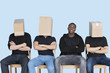 Man with friends faces covered with cardboard boxes as they sit on chairs over blue background