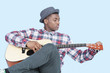Young African American man tuning guitar over light blue background