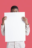 Photo : Portrait of a young man holding blank cardboard in front of face over pink background Portrait of a young man holding blank cardboard in front of face over pink background
