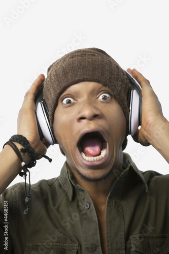 Photo: Portrait of a surprised young African American man listening music through headphones Portrait of a surprised young African American man listening music through headphones