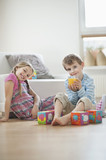 Photo: Portrait of young boy drinking orange juice while sitting with sister on floor Portrait of young boy drinking orange juice while sitting with sister on floor