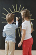 Photo : Back view of siblings drawing sun on blackboard Back view of siblings drawing sun on blackboard