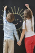 Photo : Back view of siblings drawing sun on blackboard while holding hands Back view of siblings drawing sun on blackboard while holding hands