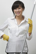 Portrait of young housemaid holding mop against gray background