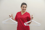Photo: Portrait of female housekeeper holding white plastic hangers against gray background Portrait of female housekeeper holding white plastic hangers against gray background