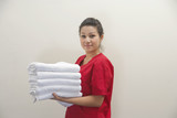 Photo: Portrait of female housekeeper holding clean white towels against gray background Portrait of female housekeeper holding clean white towels against gray background