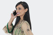 Photo: Beautiful young Indian woman in traditional wear attending phone call over gray background Beautiful young Indian woman in traditional wear attending phone call over gray background